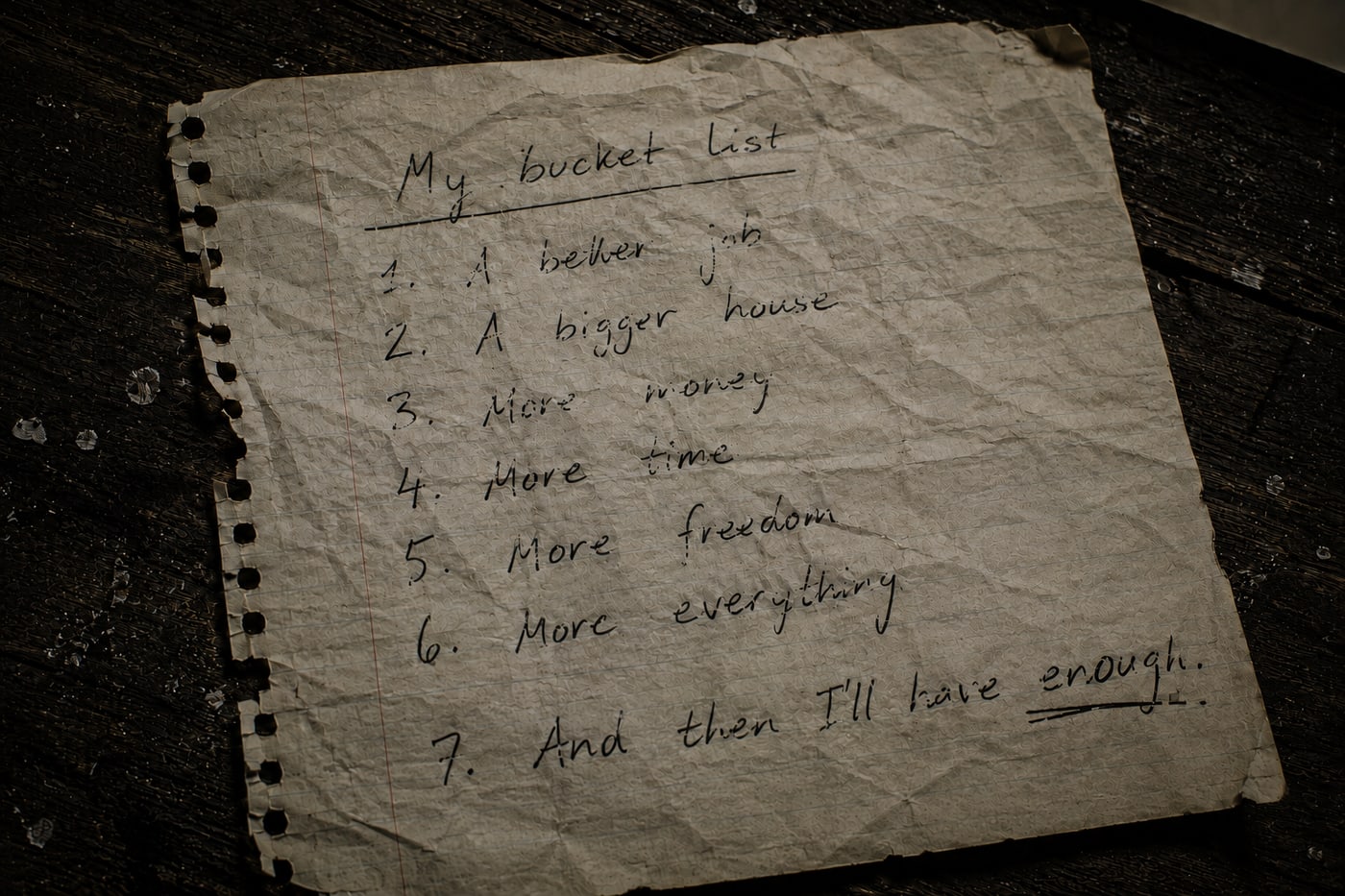 A crumpled handwritten list titled My bucket list: a better job, a bigger house, more money, more time, more freedom, more everything, and then I'll have enough.